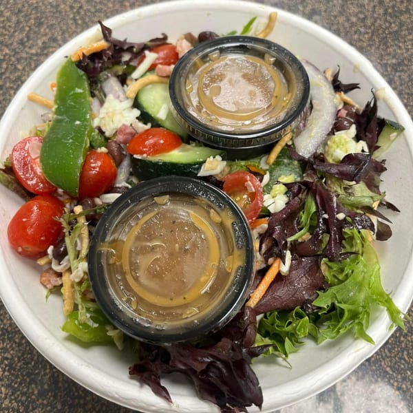 Fuel Counter's healthy salad with mixed greens, vegetables, and two dressing cups in a white bowl.