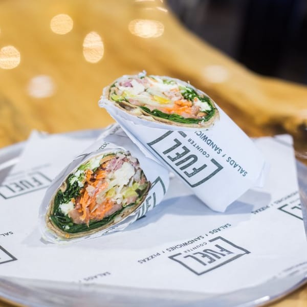 Two Fuel Counter wraps, filled with fresh vegetables and protein, on branded paper.
