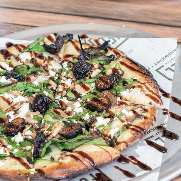 Fuel Counter's fig and goat cheese flatbread with arugula and balsamic glaze on a metal tray.